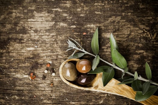 Fresh olives in a wooden spoon on a grungy textured rustic wood table with copyspace