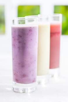 A tall glass of creamy blended yoghurt berry smoothie with a variety of other flavours in a receding row with shallow dof