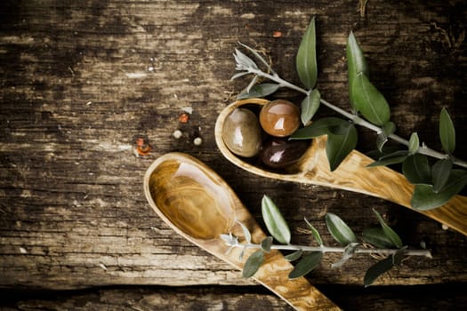Olive wood spoons with fresh olives and leaves on an old grungy textured wooden tabletop with copyspace