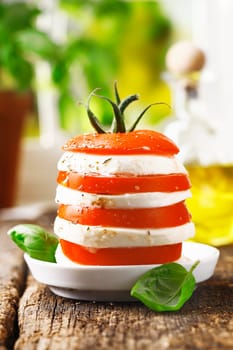 Cheese and tomato tower with alternating slices of fresh ripe red tomato and cheese served on a rustic wooden table