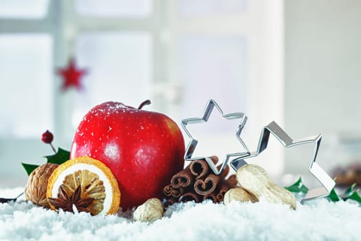 Beautiful Christmas still life with stars balanced on dried fruit, nuts and spices and a festive red apple nestling in snow with copyspace