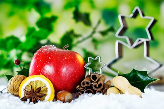 Christmas still life background with a red apple, nuts, and spices against green foliage with holly and stars