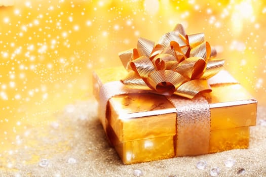 Luxury gold gift tied with a large ornamental ribbbon and bow against a golden background with copyspace for yor Christmas, Valentine, anniversary, birthday or wedding wishes