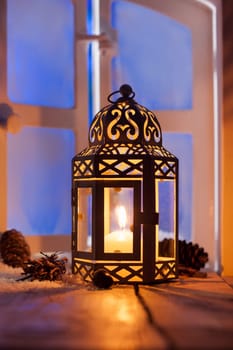 Ornamental Christmas lantern with a glowing candle illuminating a window in the evening light