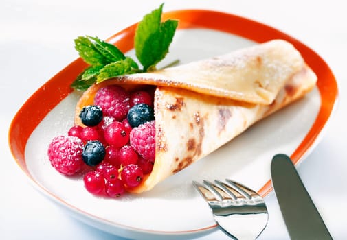 Golden panfried pancake filled with raspberries , blueberries and redcurrant dusted with sugar and served in a bowl for dessert