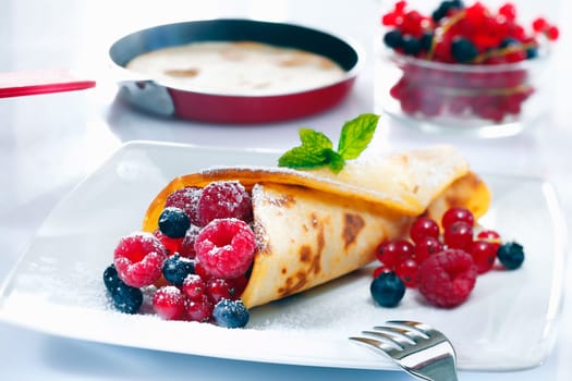 Panfried golden pancake filled with an assortment of ripe berries served in the kitchen with a pancake in a pan in the background