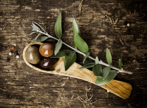 Overhead view of fresh olives in an olive wood spoon with leaves on an old wooden kitchen table