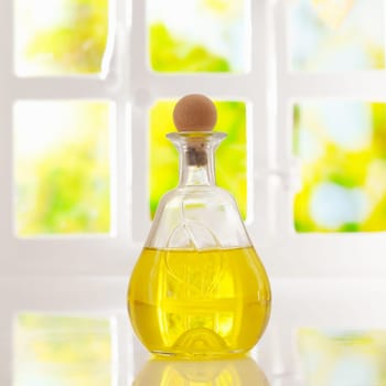 Glowing golden olive oil in a stoppered glass container for dispensing for cooking or as a salad dressing backlit by a bright airy window
