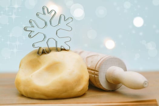 Metal snowflake cookie cutter ona pile of fresh pastry with a rolling pin alongside wating for the dough to rise before making Christmas snowflake cookies