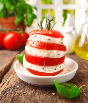 Preparing an individual gourmet cheese and tomato salad with a tower formed of alterning slices standing on a rustic wooden kitchen table
