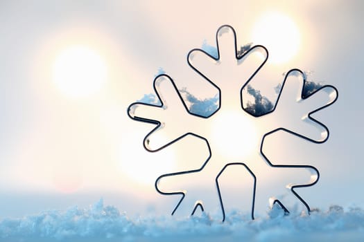 Outline of a metal snowflake cookie cutter on a bed of blue snow with a bokeh of glowing lights and copyspace for your Christmas greeting