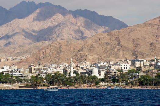 Seaside view of the jordan city of Aqaba at the Red Sea. Deep blue sea,white buildings,green trees and majestic hills.