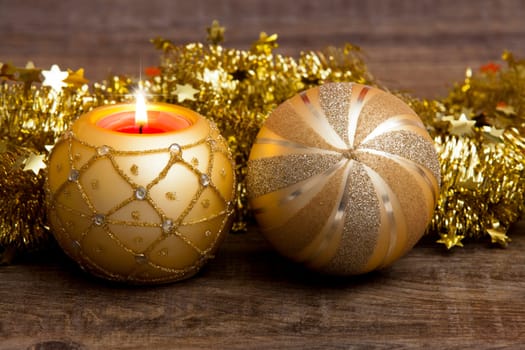 Candle in golden candle holder and golden Christmas tree ball with gold garland on wooden background