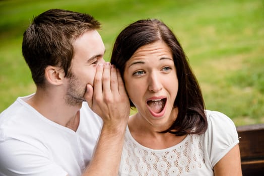 Young man whispering to woman (girlfriend) - surprise expression