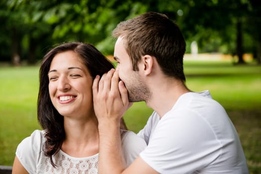 Young man whispering to woman (girlfriend) - outdoor lifestyle photo