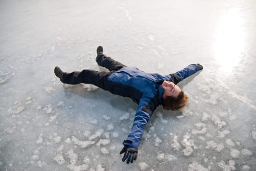 Young smiling woman is lying on ice (frozen lake) - winter outdoor scene