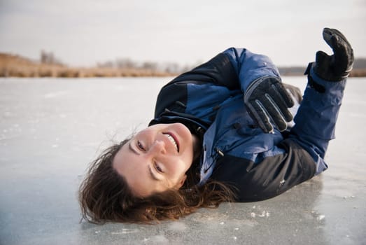 Young smiling woman is lying on ice (frozen lake) - winter outdoor scene