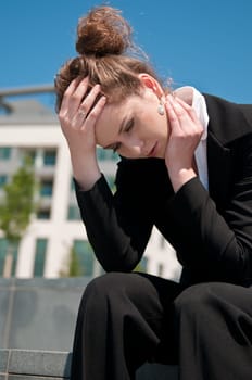 Young worried business woman siting outdoors - head in hand