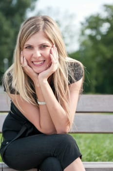 Portrait of young beautiful smiling woman siting on bench in park outside