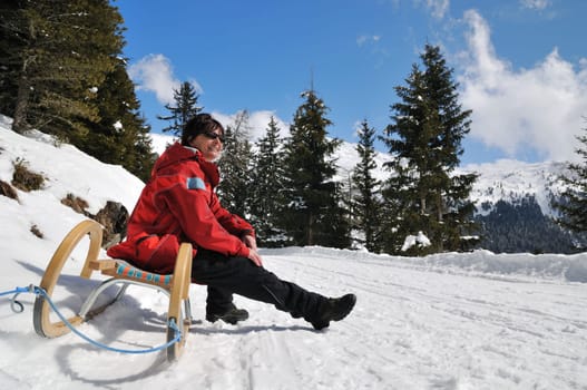 Senior woman siting on sledge sunning in mountain winter snow country with blue sky