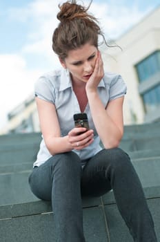 Young unhappy woman typing on mobile phone - outdoors in street