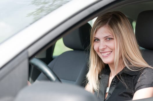 Young beautiful smiling woman driving car - portrait through side window