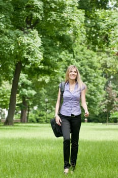 Young business woman wit laptob bag walking outdoors in park