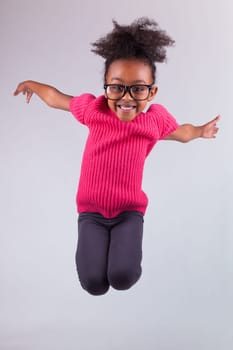 Portrait of cute Young African American girl jumping, over gray background