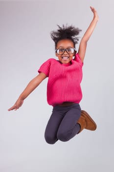 Portrait of cute Young African American girl jumping, over gray background