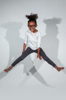Portrait of cute Young African American girl jumping, over gray background