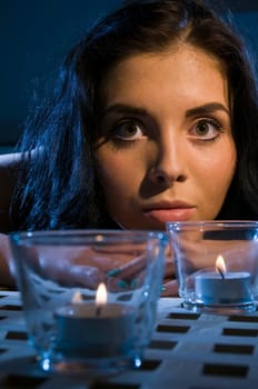 Head and shoulders shot of a young black-haired woman with her head propped up on the table and two tea lights in the blurred foreground