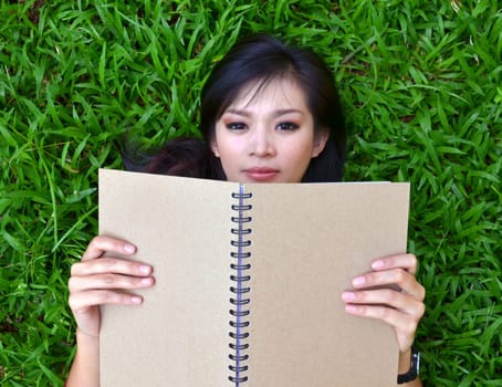 Woman lying on green grass with a book