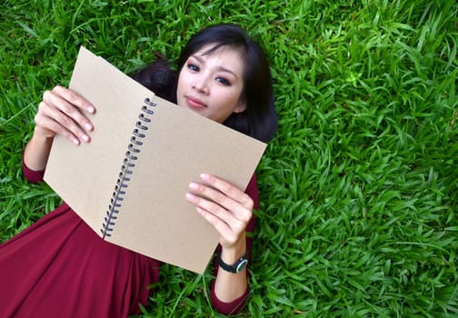 Woman lying on green grass with a book