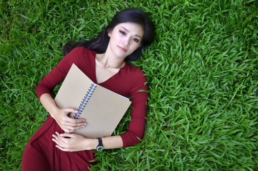 Woman lying on green grass with a book