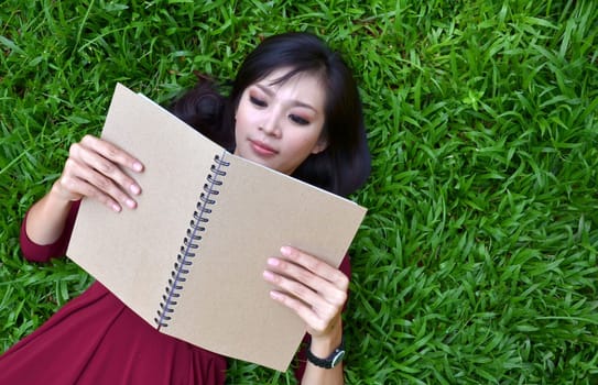Woman lying on green grass with a book