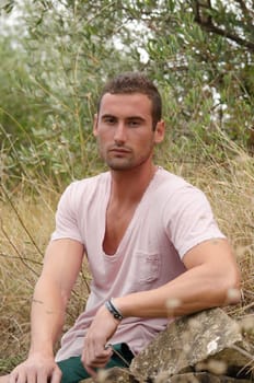 Good looking male model sitting on rock in a field