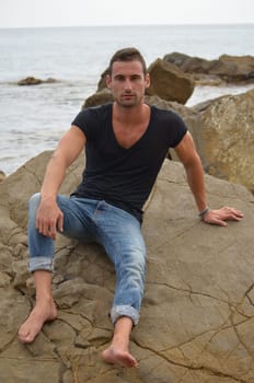 Handsome and fit young man on rock by the sea