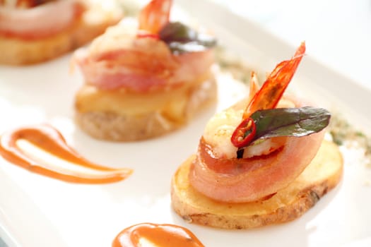 Delicious and delicate shrimps wrapped in bacon on potato slices with a spinach leaf.