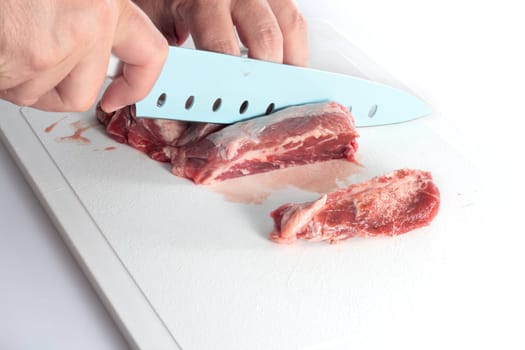 cutting of pork meat with kitchen knife on white background