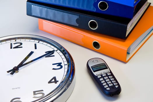 Clock, phone and color binders on the office desk,