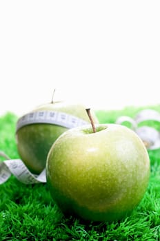 Two apples close up on the grass and one with a tape measure