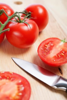 Fresh tomatoes being sliced on a wooden chopping board with knife