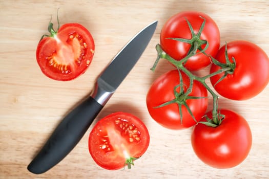 Fresh tomatoes being sliced on a wooden chopping board with knife