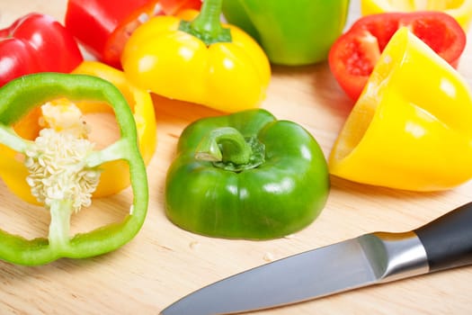 Selection of red green and yellow peppers sliced up on a chopping board