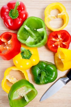 Selection of red green and yellow peppers sliced up on a chopping board