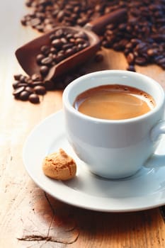 Morning cup of frothy espresso coffee on a wooden table made with freshly ground roasted coffee beans seen in the background spilling from a scoop