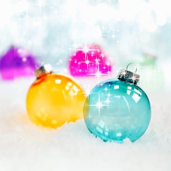 Sparkling twinkling colourful translucent glass Christmas baubles in fresh winter snow with bokeh of soft white lights, square format
