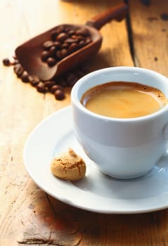Strong aromatic espresso coffee served in a small cup with a macaroon on the side and a scoop of coffee beans in the background