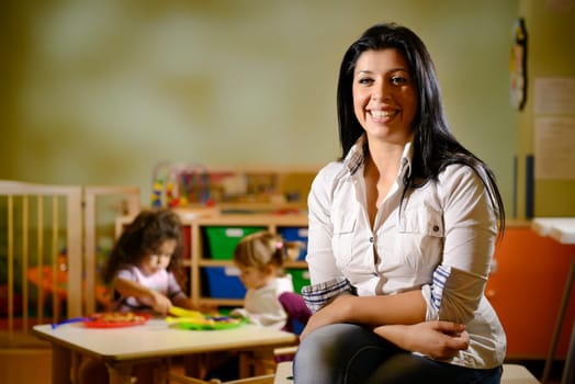 Portrait of female teacher smiling at camera and happy children eating lunch at school. Copy space