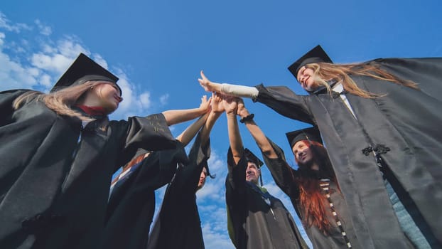 Graduates in black school uniforms join hands. The concept of team and strong friendship